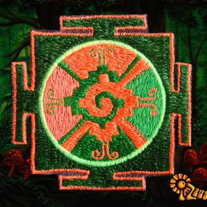 May include: Embroidered patch featuring a central circular design with orange and green geometric patterns. The patch has a square border and is set against a forest backdrop with red mushrooms and the text "Zauberwald".