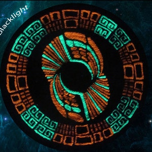 May include: Circular blacklight design with orange and teal geometric patterns. The design features a central figure with symmetrical shapes and the word "blacklight" in white text. The background is a dark blue space scene.
