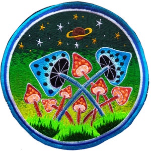 May include: Embroidered patch featuring a whimsical design. The patch showcases a vibrant scene with orange and blue mushrooms, a starry sky, and a planet. The design is set within a circular border with shades of green and blue.