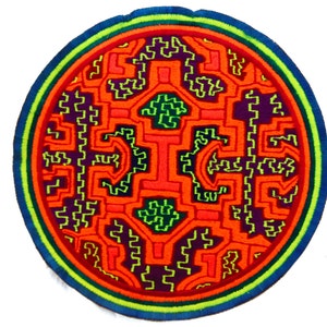 Pode incluir: Um patch redondo bordado com um design geométrico complexo. O padrão central é laranja com detalhes verdes e roxos, rodeado por uma borda azul, verde e laranja. Adequado para roupas ou acessórios.