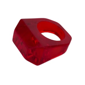 May include: A vibrant red, geometric ring with a square shape and a circular opening. The ring is made of a translucent material, showcasing its internal structure. The design is modern and eye-catching.