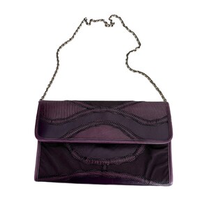 May include: A purple quilted clutch bag with a silver chain strap. The bag has a unique design with a quilted pattern and a flap closure.