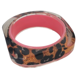 May include: A square-shaped bangle bracelet with a pink interior and a leopard print design in black, brown, and gold.