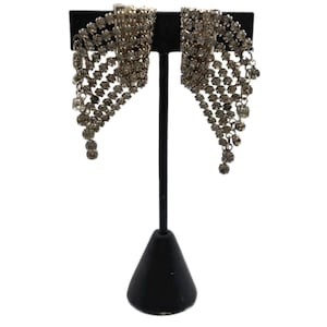 May include: A pair of silver-toned dangle earrings featuring a cascading, fan-shaped design composed of multiple rows of clear, faceted rhinestones. The earrings have a flexible, mesh-like structure that tapers toward the bottom.