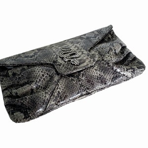 May include: A gray snakeskin clutch with a silver snake charm embellished with rhinestones.