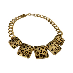 May include: A gold chain necklace with five square-shaped pendants. Each pendant is decorated with a leopard print pattern and has small, dark brown rhinestones.