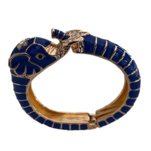 May include: A hinged bracelet featuring an elephant design. The bracelet is primarily gold-toned with a dark blue enamel finish. The elephant heads are adorned with clear rhinestones, adding a touch of sparkle to the jewelry.