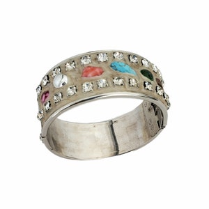 May include: A silver bangle bracelet with a white enamel base and colorful stones. The stones are set in a row around the bracelet and include turquoise, red, green, and pink.