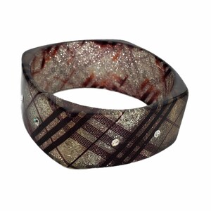 May include: A brown and silver bangle bracelet with a plaid pattern and clear rhinestones.