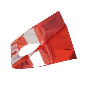 May include: A red and clear acrylic ring with a geometric shape. The ring has a wide band and a square-shaped top.