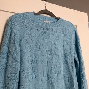 May include: A light blue sweater with a textured pattern. The sweater has a crew neck and long sleeves.