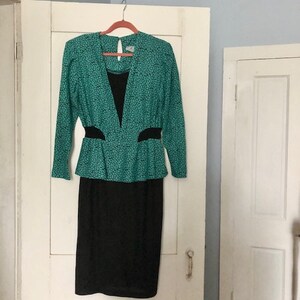 May include: A two-piece dress with a green and black patterned top and a black skirt. The top has a V-neckline and a fitted waist. The skirt is knee-length and has a straight silhouette.