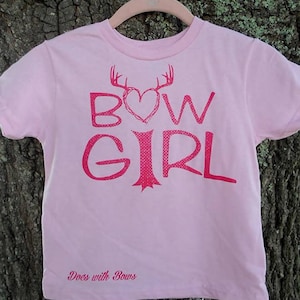May include: Pink t-shirt with a red graphic of a heart with antlers and the text "BOW GIRL" and the text "Does with Bows" at the bottom.