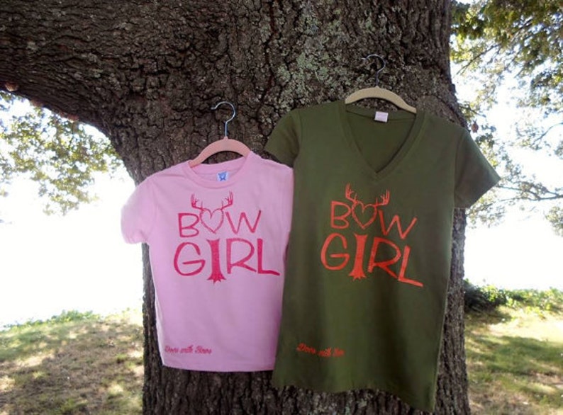 May include: Two pink and green t-shirts with the text "BOW GIRL" and a heart with antlers above the word "BOW". The text is in red and the shirts have the words "Love with Love" printed on the bottom.