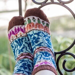 May include: A pair of colourful knitted socks with a brown cuff and a blue, white, pink and orange pattern. The socks are resting on a black metal railing.