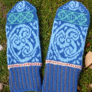May include: A pair of blue knitted mittens with a white and green patterned design. The mittens have a ribbed cuff and a decorative band of red, white, and cream.