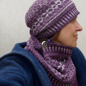 May include: A purple and white knitted hat and matching scarf. The hat has a geometric pattern and the scarf is folded around the neck.