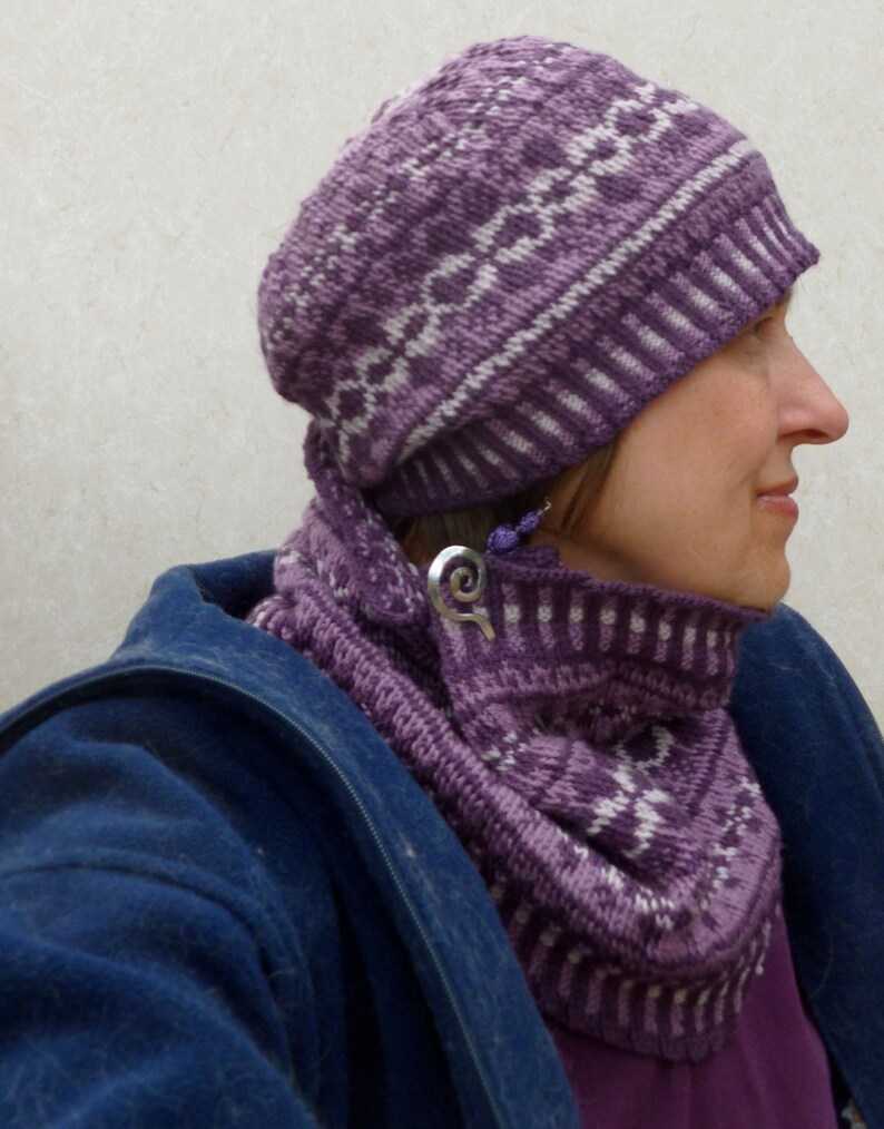 May include: A purple and white knitted hat and matching scarf. The hat has a geometric pattern and the scarf is folded around the neck.