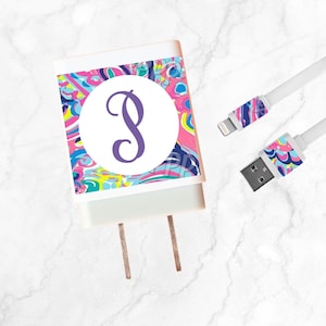 May include: White phone charger with a colorful abstract pattern in pink, blue, and yellow. The charger features a large white circle with a purple letter "B". A matching white charging cable is also included.