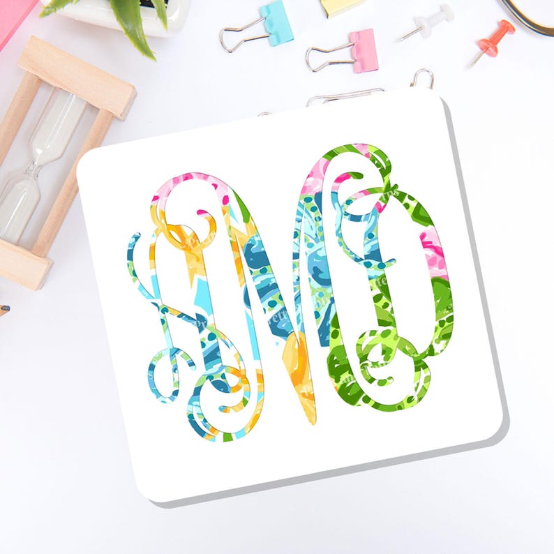 May include: A square white coaster featuring a large, decorative, interlocking monogram letter M. The letter is filled with a vibrant, multi-colored abstract pattern consisting of shades of bright green, blue, yellow, and pink in a swirling design.