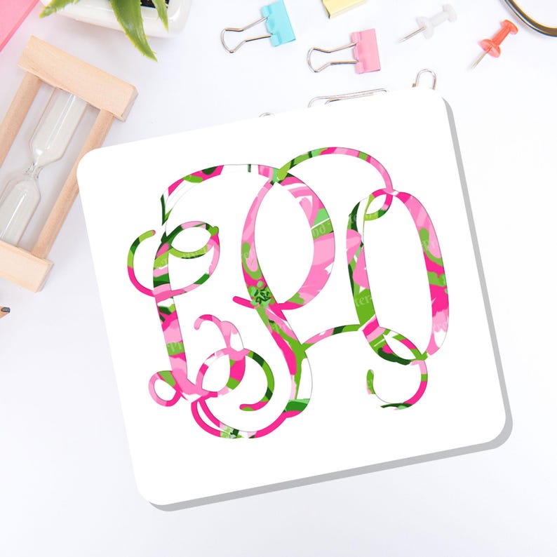 May include: A square white coaster featuring a large, stylized monogram with a vibrant floral pattern in shades of hot pink, light pink, and bright green. The letters are intertwined in a decorative script font, creating a bold, colorful focal point.