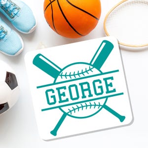 May include: A white square with a teal baseball design and the name "GEORGE" in teal block letters. A basketball, soccer ball, tennis racket, and blue sneakers are also visible.