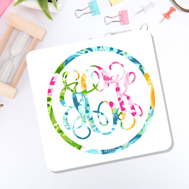 May include: A square white coaster featuring a circular design in the center. The design consists of a colorful, multi-patterned monogram enclosed within a circular border that matches the vibrant, abstract floral and geometric print of the letters.