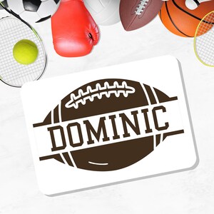 May include: A white rectangular sticker featuring a brown football design with the name "DOMINIC" in bold, white letters. The sticker is surrounded by sports equipment, including a tennis racket, a basketball, and a football.