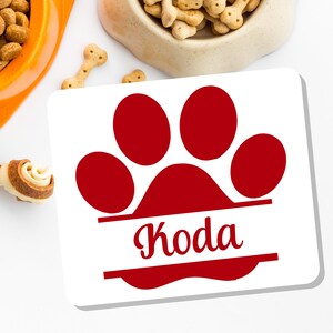 May include: White ceramic tile with a red paw print and the name "Koda" written in a red cursive font.