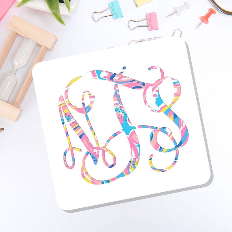 May include: A square white coaster featuring a decorative, swirling monogram design in the center. The letters are filled with a vibrant, multi-colored pattern consisting of pink, blue, yellow, and white abstract shapes and wavy lines.