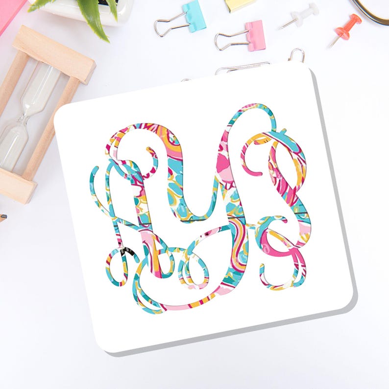 May include: A square white coaster featuring a large, ornate, interlocking monogram letter design. The monogram is filled with a vibrant, multi-colored paisley-inspired pattern in shades of bright pink, turquoise blue, yellow, and orange.