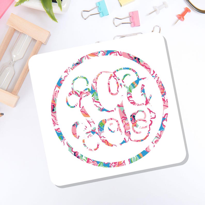 May include: A square white coaster featuring a circular monogram design filled with a vibrant, multi-colored floral and abstract pattern in shades of pink, blue, orange, and green. The letters within the circular frame are stylized and interconnected.