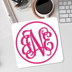May include: A white coaster with a pink circle containing a pink monogram of the letter "N".