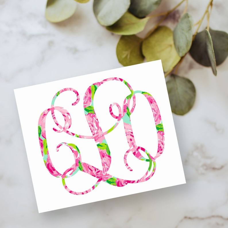 May include: A decorative monogram sticker featuring three intertwined letters in a vibrant floral pattern. The design displays a mix of bright pink, green, and light blue colors in a swirling, cursive script style set against a plain white background.