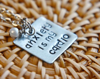Könnte beinhalten: Eine silberne Halskette mit einer kleinen weißen Perle und einem quadratischen Anhänger mit der Aufschrift "Angst ist mein Cardio".
