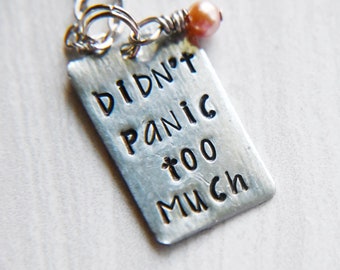 Könnte beinhalten: Eine silberne Halskette mit einem Anhänger, auf dem "Didn't Panic Too Much" steht. Der Anhänger ist an einer silbernen Kette mit einer kleinen rosa Perle befestigt.
