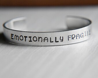 Könnte beinhalten: Ein silbernes Armband mit der Gravur "Emotional Fragile".