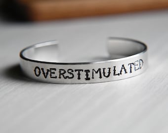 Könnte beinhalten: Ein silbernes Armband mit der Gravur "Overstimulated".