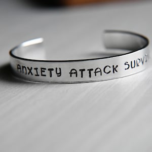 Könnte beinhalten: Ein silbernes Armband mit der Gravur "Anxiety Attack Survivor".