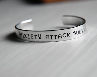 Könnte beinhalten: Ein silbernes Armband mit der Gravur "Anxiety Attack Survivor".
