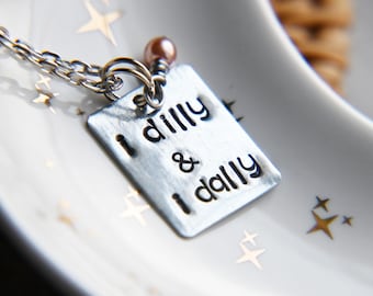 Könnte beinhalten: Eine silberne Halskette mit einem Anhänger, auf dem "I dilly & I dally" steht.