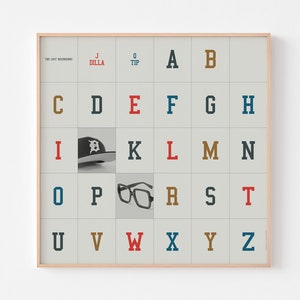 May include: A framed alphabet poster with a light gray background and a grid of white squares. Each square contains a letter of the alphabet in a different color. The letters A, B, C, D, E, F, G, H, I, J, K, L, M, N, O, P, Q, R, S, T, U, V, W, X, Y, and Z are displayed. The letters are in a variety of colors, including red, blue, green, yellow, and brown. The letter D is replaced with a black and white baseball cap. The letter Q is replaced with a pair of black glasses. The poster is framed in a light wood frame.