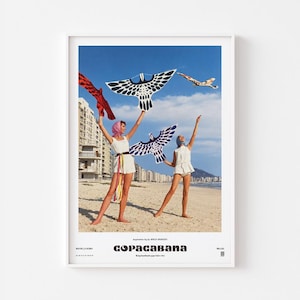 May include: A framed poster featuring a beach scene with two individuals in white outfits holding bird-shaped kites. The text reads Copacabana, Rio de Janeiro, and BR-LTD. The kites are black, white, and red against a clear blue sky and sandy beach.
