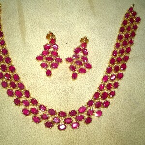 May include: A gold necklace and earrings set with a double row of oval-shaped ruby stones.