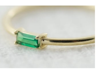 May include: A delicate gold ring with a single emerald green baguette-shaped gemstone set in the band.