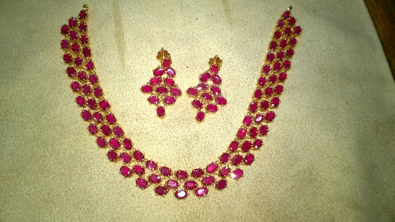 May include: A gold necklace and earrings set with a double row of oval-shaped ruby stones.