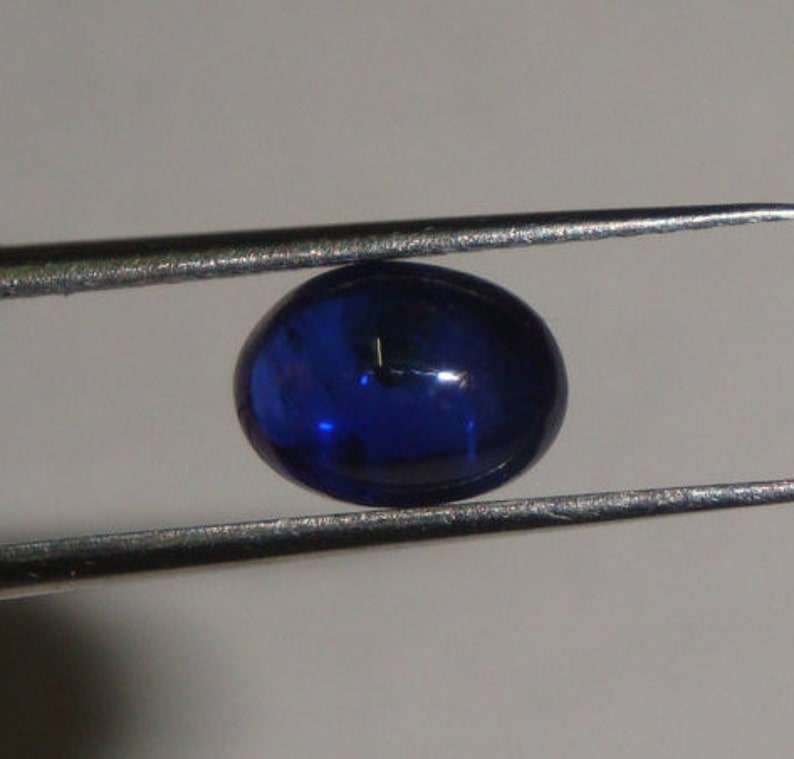 May include: A deep blue oval cabochon gemstone, held in a pair of tweezers.