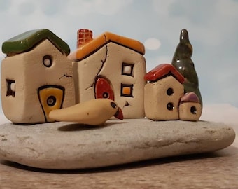 Ceramic village of white clay houses with a little clay bird and a tree on natural beach stone, Fine art small sculpture