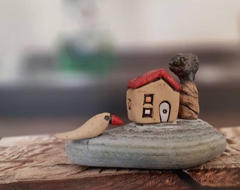 Fine art piece of a ceramic house with a miniature bird and a tree on a natural beach stone