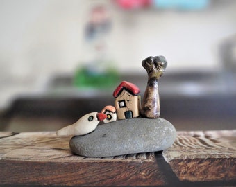 Ceramic gift of a miniature including two little clay houses, a tree and a dove on a gray beach stone. Whimsical unique gift